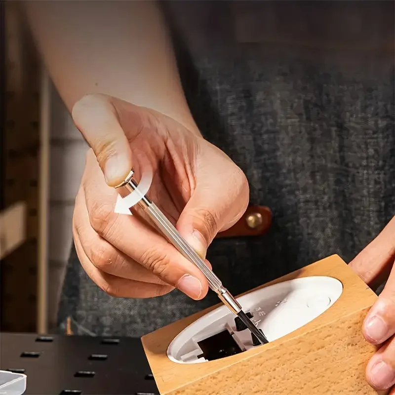 Mano utilizando un destornillador de precisión en un reloj de madera mostrando el giro superior.