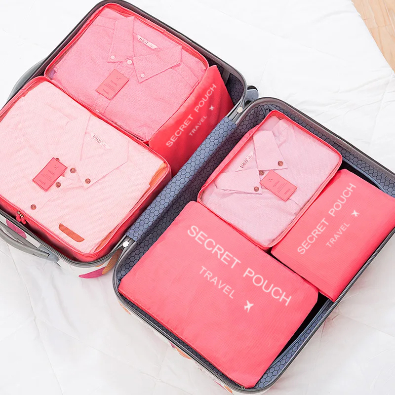Vista superior de maleta abierta con camisas ordenadas dentro de cubos y sobres rosados.